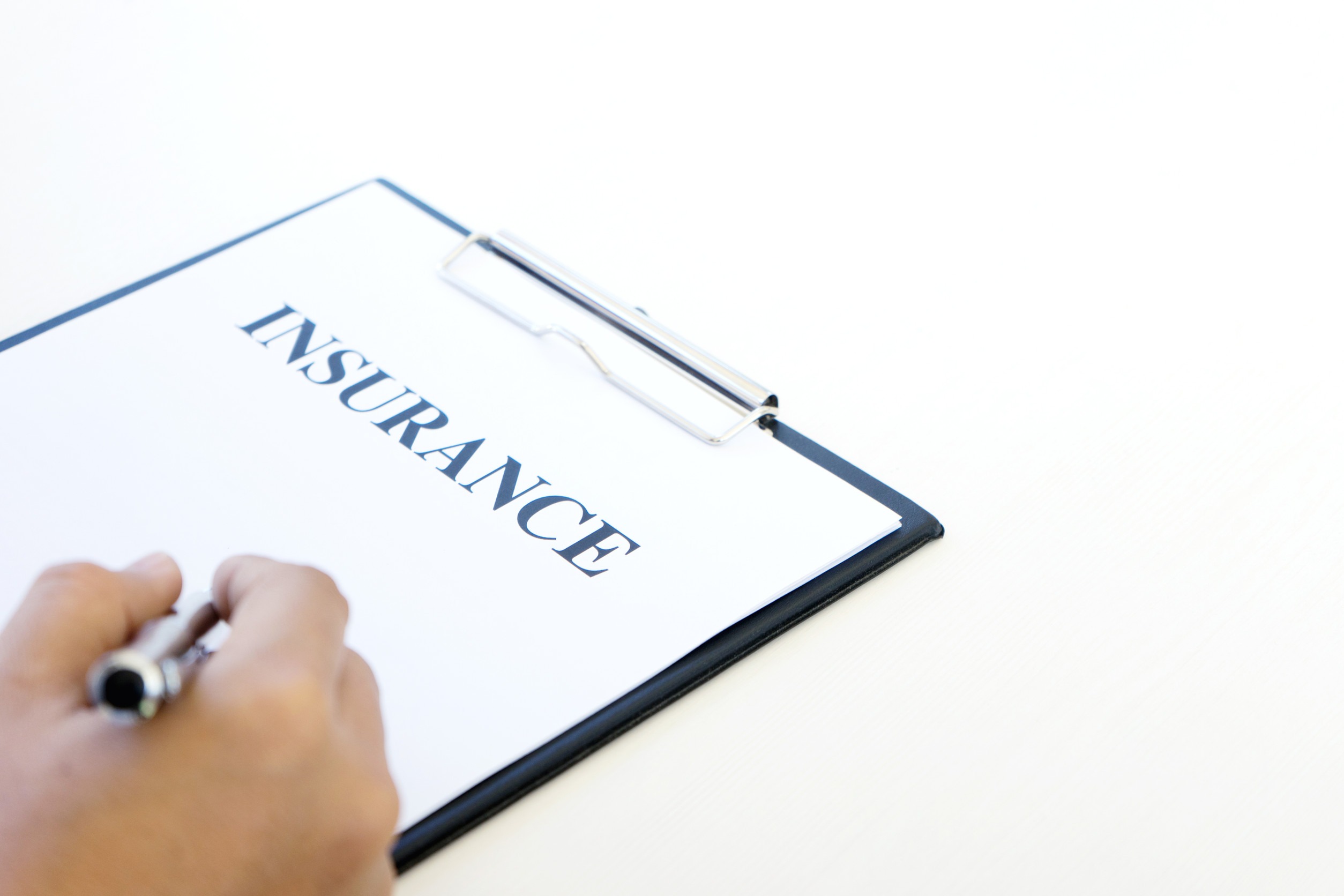 A hand holding a pen is about to write on a clipboard with a document titled 